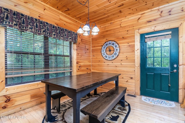 dining area featuring an inviting chandelier, wood ceiling, wooden walls, and light wood-type flooring