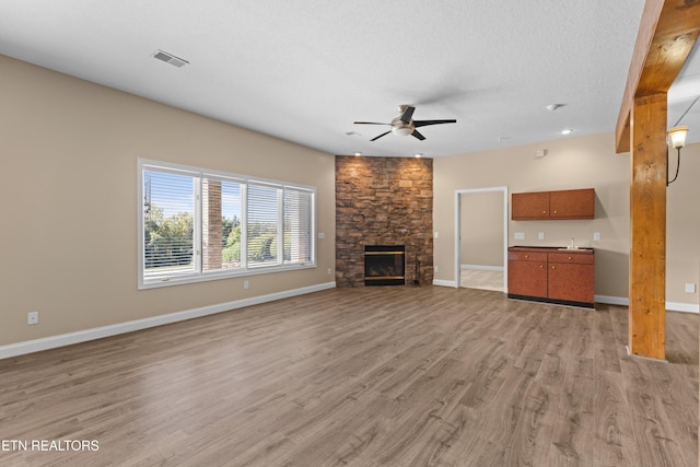 unfurnished living room with a textured ceiling, a fireplace, light hardwood / wood-style floors, and ceiling fan