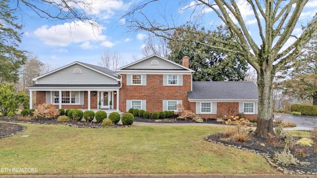 view of front facade featuring covered porch, brick siding, a chimney, and a front yard