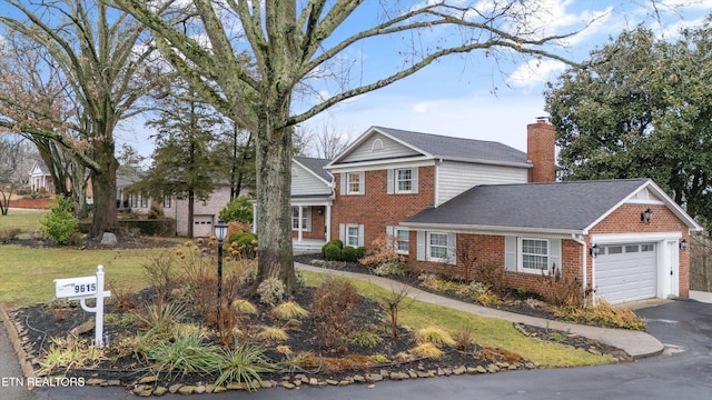 traditional-style house featuring driveway, a chimney, an attached garage, a front lawn, and brick siding