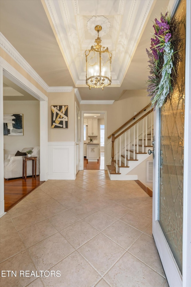 tiled foyer entrance with ornamental molding, an inviting chandelier, and a tray ceiling