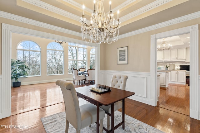 dining area featuring light hardwood / wood-style flooring, ornamental molding, a raised ceiling, and a chandelier