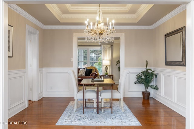 dining space with a tray ceiling, a wainscoted wall, a notable chandelier, and wood finished floors