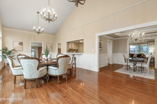 dining space with an inviting chandelier, high vaulted ceiling, ornamental molding, and light hardwood / wood-style floors