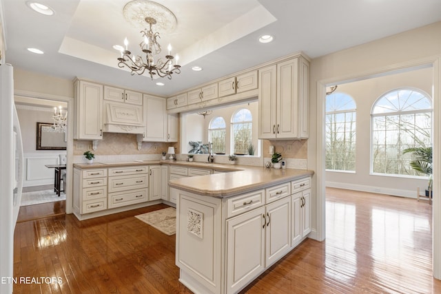 kitchen featuring an inviting chandelier, a tray ceiling, kitchen peninsula, and hanging light fixtures