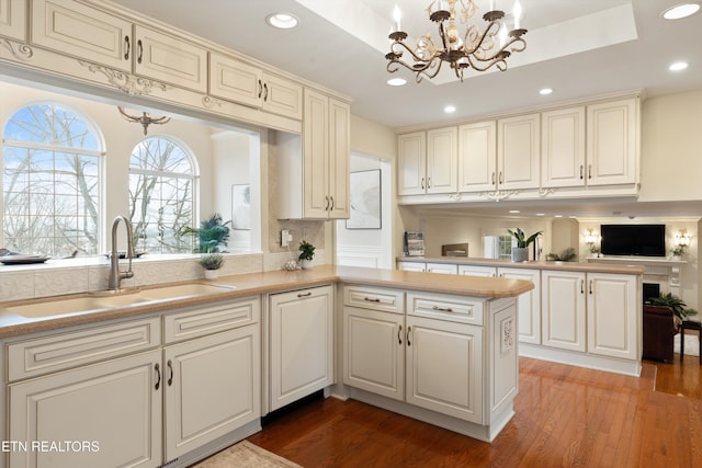 kitchen with a peninsula, a sink, light countertops, light wood-type flooring, and a raised ceiling