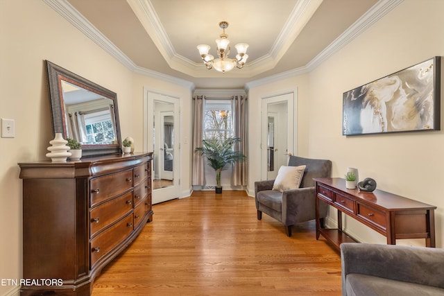 living area with ornamental molding, a chandelier, a raised ceiling, and light wood-type flooring