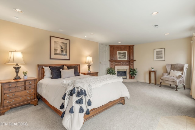 bedroom featuring light carpet, a glass covered fireplace, visible vents, and recessed lighting