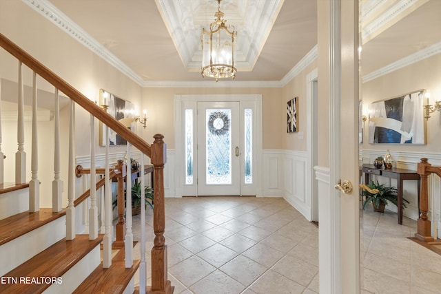 foyer with stairway, a raised ceiling, crown molding, and a decorative wall