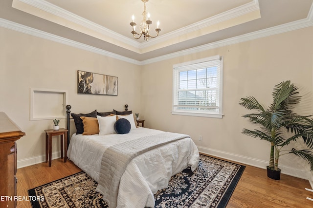 bedroom featuring a raised ceiling, ornamental molding, wood finished floors, a chandelier, and baseboards