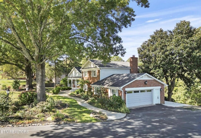 traditional-style house featuring a garage, a chimney, aphalt driveway, and brick siding