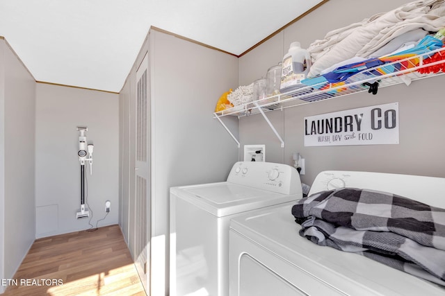 clothes washing area featuring ornamental molding, washing machine and clothes dryer, and light hardwood / wood-style floors