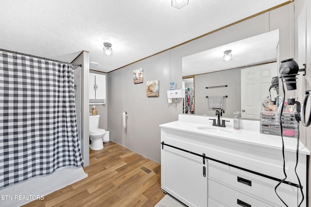 bathroom featuring hardwood / wood-style flooring, vanity, ornamental molding, toilet, and a textured ceiling