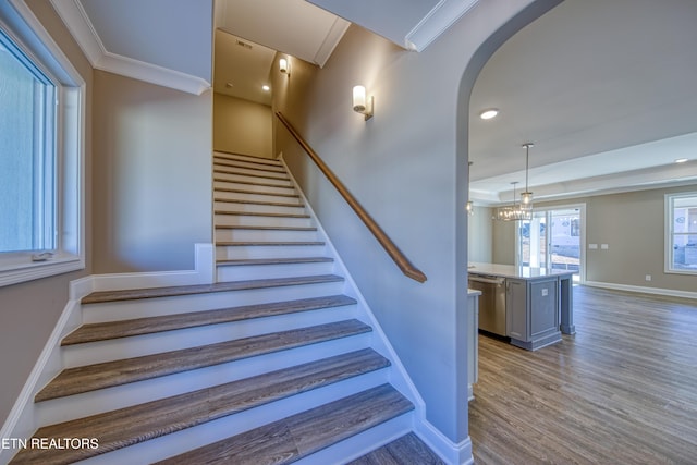 stairway featuring hardwood / wood-style flooring, crown molding, and a notable chandelier