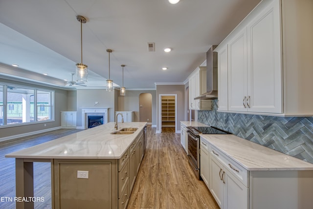 kitchen featuring decorative light fixtures, sink, stainless steel range with electric cooktop, a large island, and wall chimney range hood