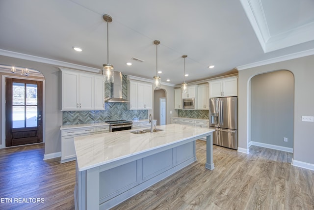 kitchen with sink, wall chimney range hood, appliances with stainless steel finishes, white cabinets, and decorative light fixtures