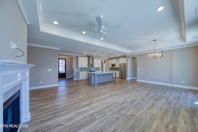 unfurnished living room featuring ornamental molding, ceiling fan with notable chandelier, light hardwood / wood-style flooring, and a tray ceiling