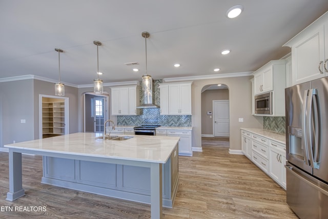 kitchen featuring decorative light fixtures, an island with sink, sink, stainless steel appliances, and wall chimney range hood