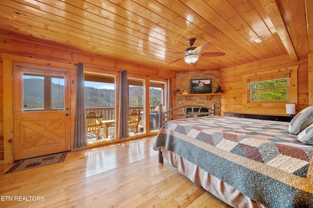 bedroom with wooden walls, a fireplace, access to outside, light hardwood / wood-style floors, and wooden ceiling