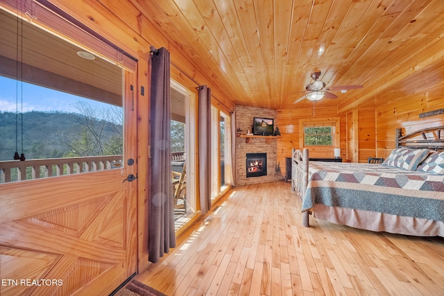 bedroom featuring access to outside, wooden ceiling, wooden walls, a fireplace, and light hardwood / wood-style floors