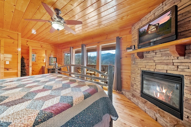 bedroom with wood ceiling, an outdoor stone fireplace, light wood-type flooring, and wood walls