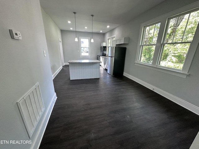 kitchen with pendant lighting, appliances with stainless steel finishes, white cabinetry, dark hardwood / wood-style floors, and a kitchen island