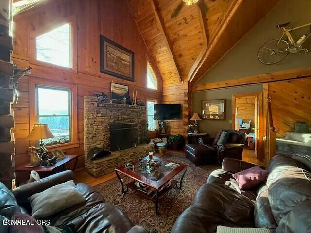 living room featuring wooden ceiling, high vaulted ceiling, a fireplace, and wooden walls