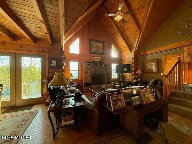 living room featuring beam ceiling, wood ceiling, a stone fireplace, and wood-type flooring