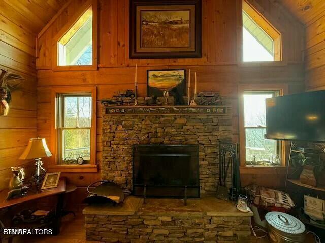 living room featuring a stone fireplace, a wealth of natural light, high vaulted ceiling, and wood walls