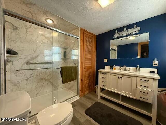 bathroom featuring hardwood / wood-style floors, a shower with shower door, vanity, toilet, and a textured ceiling