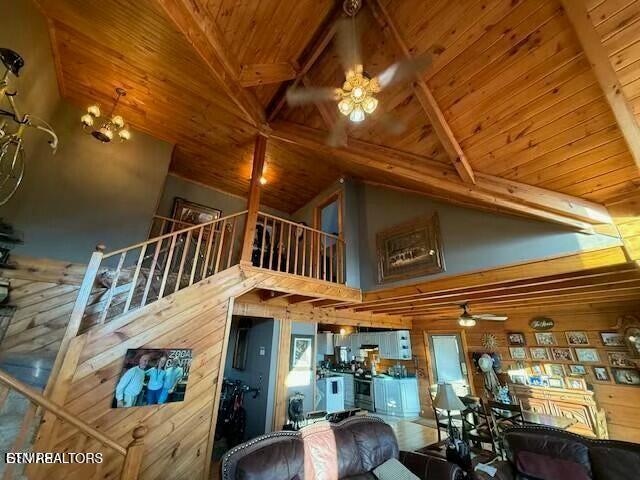 unfurnished living room with high vaulted ceiling, beam ceiling, wooden ceiling, and wood walls