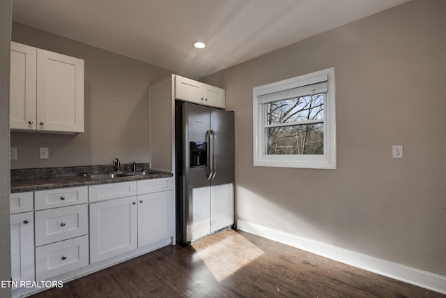 kitchen featuring sink, dark wood-type flooring, stainless steel fridge, white cabinets, and dark stone counters