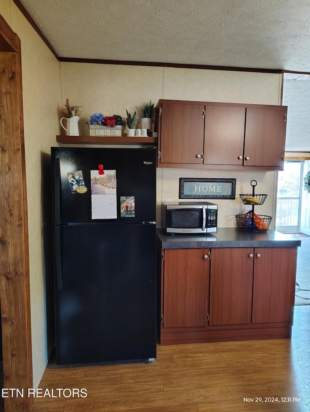 kitchen with crown molding, black fridge, a textured ceiling, and light wood-type flooring