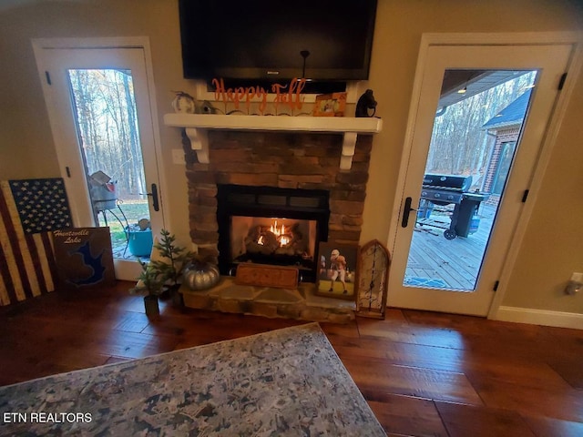 living area with a stone fireplace and dark wood-type flooring