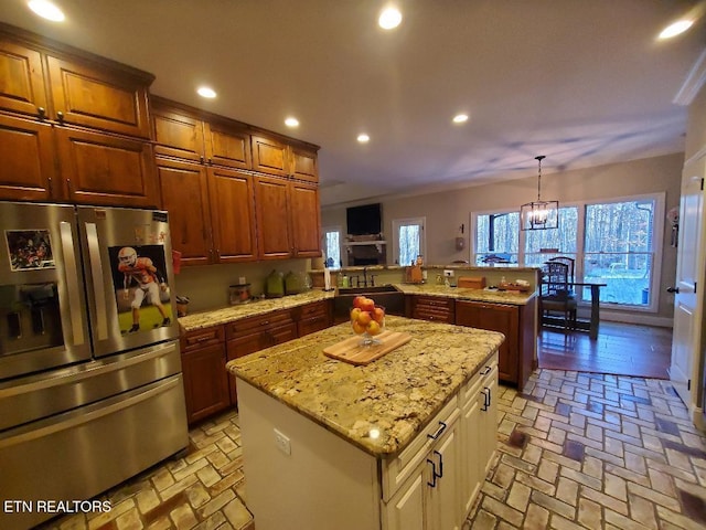 kitchen with sink, stainless steel fridge, hanging light fixtures, a center island, and light stone countertops