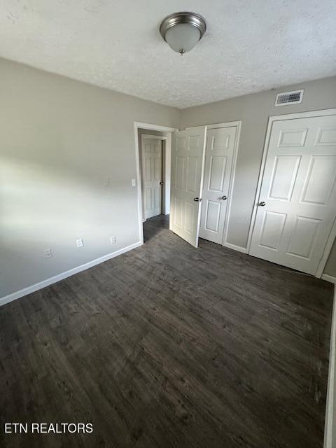 unfurnished bedroom featuring multiple closets, dark wood-type flooring, and a textured ceiling