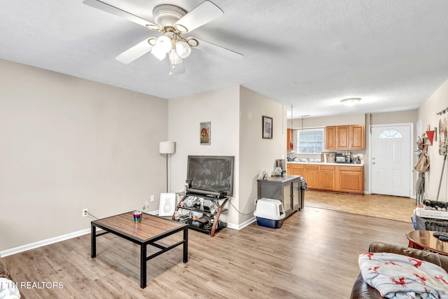 living room with ceiling fan, a textured ceiling, and light wood-type flooring