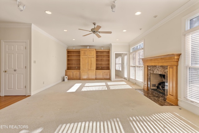 unfurnished living room featuring crown molding, ceiling fan, a high end fireplace, and light carpet