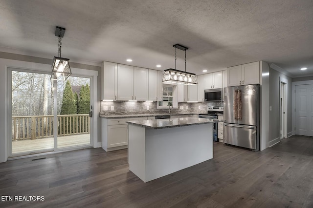 kitchen featuring stainless steel appliances, white cabinets, dark stone counters, and decorative light fixtures