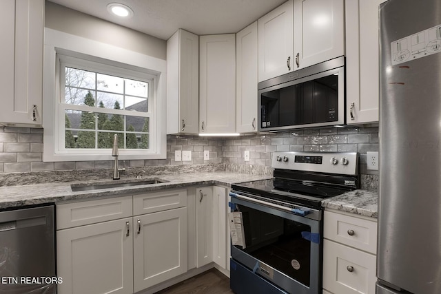 kitchen with sink, appliances with stainless steel finishes, light stone countertops, white cabinets, and decorative backsplash