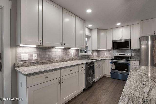 kitchen with sink, dark wood-type flooring, appliances with stainless steel finishes, light stone counters, and white cabinets