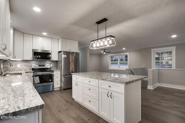 kitchen featuring sink, hanging light fixtures, stainless steel appliances, a center island, and white cabinets