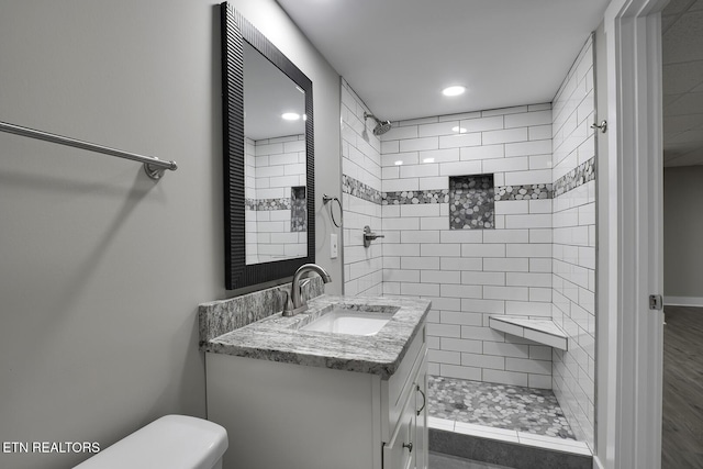 bathroom with vanity, toilet, hardwood / wood-style floors, and a tile shower