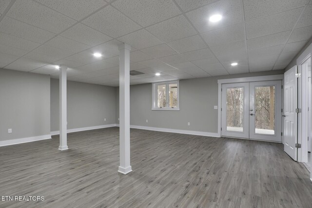 basement featuring hardwood / wood-style floors, a paneled ceiling, and french doors