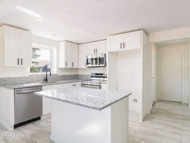 kitchen featuring light stone counters, a kitchen island, white cabinets, and appliances with stainless steel finishes