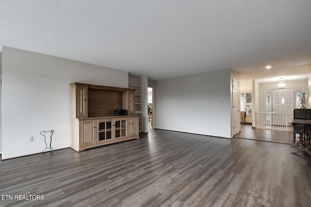 unfurnished living room with a notable chandelier, dark wood-type flooring, and a textured ceiling