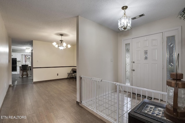 entryway featuring wood-type flooring, a textured ceiling, and an inviting chandelier