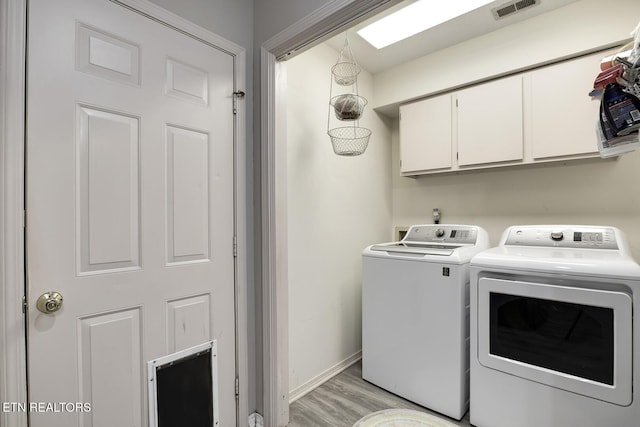 clothes washing area featuring cabinets, washer and clothes dryer, and light hardwood / wood-style flooring