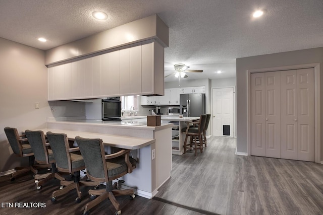 kitchen with sink, hardwood / wood-style flooring, appliances with stainless steel finishes, white cabinets, and kitchen peninsula