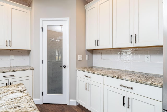 kitchen featuring white cabinetry, dark parquet flooring, light stone counters, and backsplash